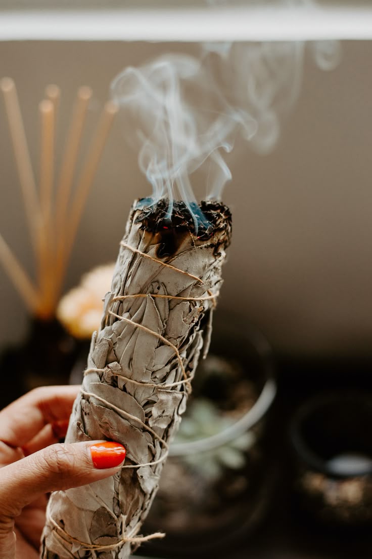 Person holding a smoldering sage bundle with smoke rising, blurred background